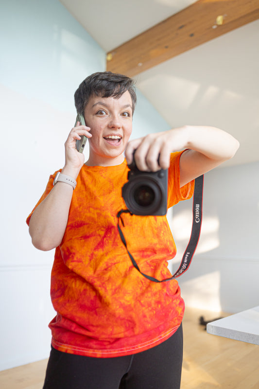 Corky taking a picture of herself wearing a bright orange shirt.